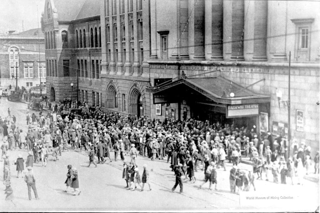 Parkway Theater (also known as Fox, Silver Bow, Masonic, Temple) matinee - crowd leaving, Butte, MT. Old Butte High School is the second building from the theater. Now the Mother Lode Theater. Circa 1920