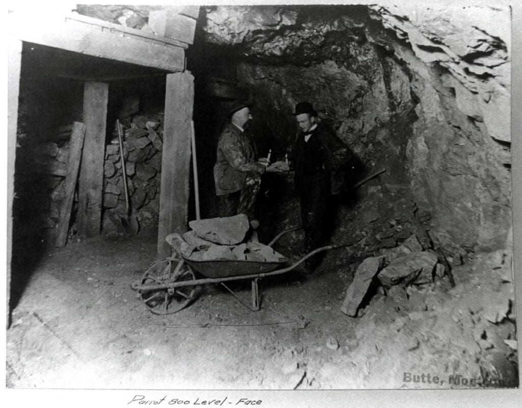 Image taken underground in the Parrot Mine with two miners using candles to examine rock. The view is at the 800-foot level. The men are most likely supervisors since their garb is not that of the regular miner. Circa 1898