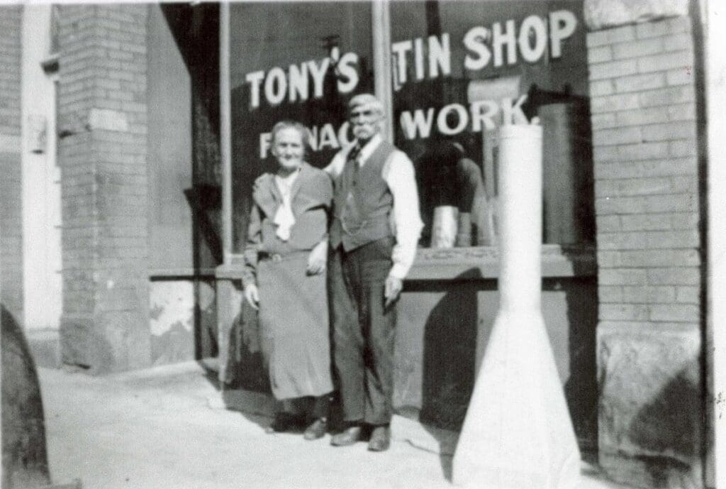 Picture of Tony's Tin Shop. Butte, MT with Antonio (Tony) and Myra Canonica standing in front. The second floor of this building is known as the Myra, named for Myra Canonica. Circa 1920